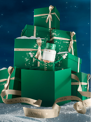 Multiple green La Mer gift boxes stacked in a winter setting, draped in gold ribbons