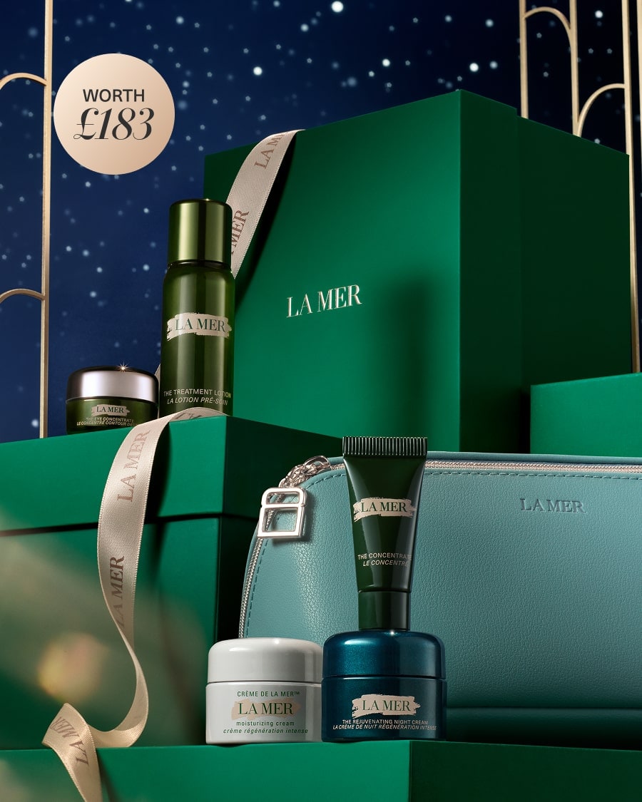 Selection of La Mer deluxe minis and makeup bag, nested on green decorated La Mer gift boxes, in dramatic, wintering lighting